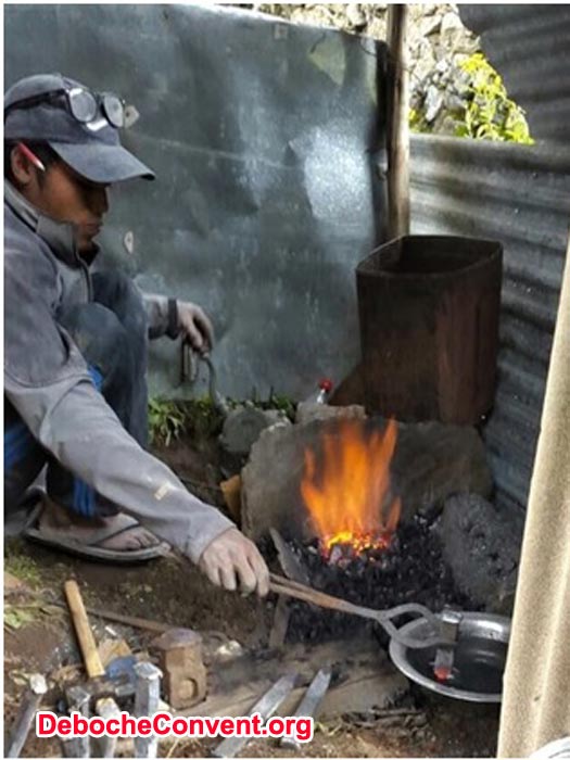 A worker forges metal stakes over a wood fire.